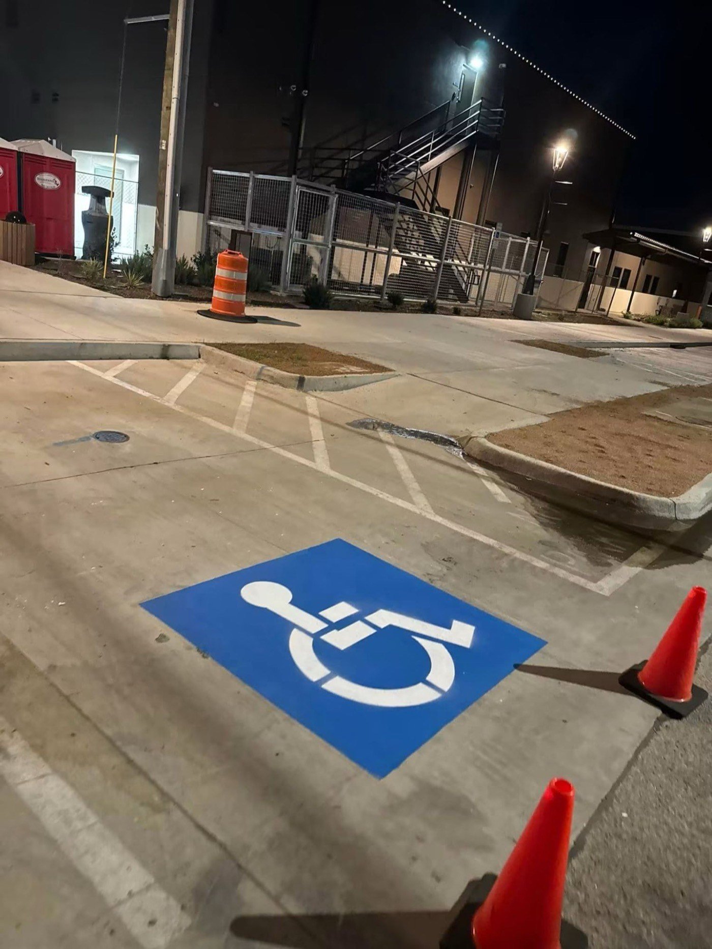 Newly painted blue and white accessible parking symbol on concrete, marked out at night with traffic cones