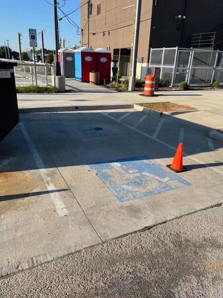 Worn and faded accessible parking symbol on a concrete bay marked with a traffic cone before repainting