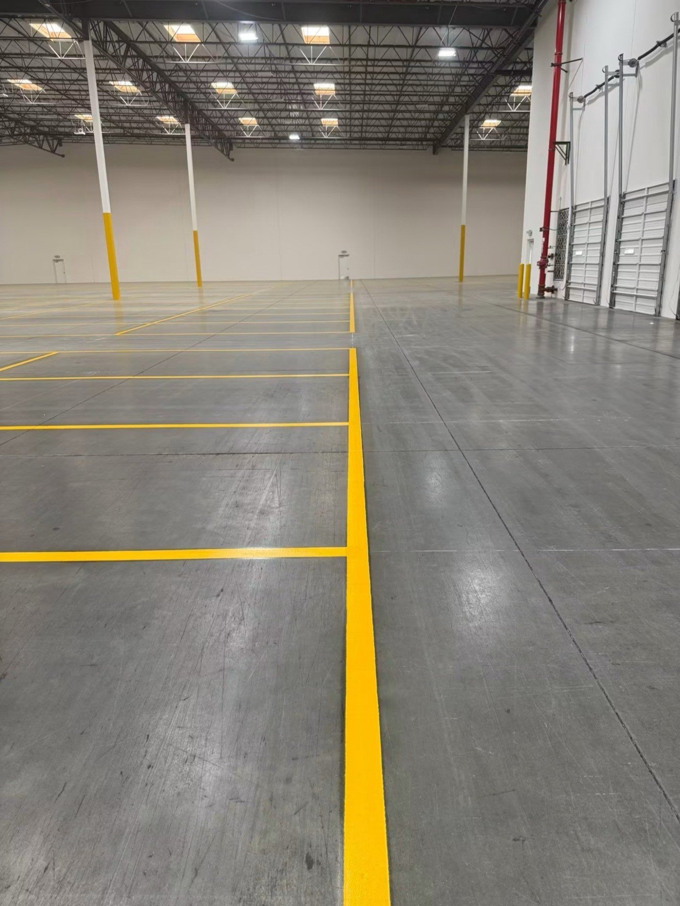 Yellow line grid marked across a large warehouse floor with yellow-painted support bollards