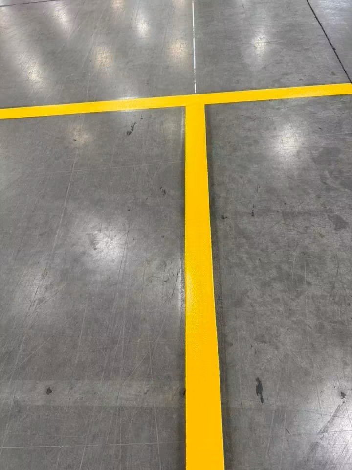 Close view of a crisp yellow T-junction line painted on a concrete warehouse floor